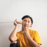 Pensive ethnic man listening to answer in paper cup phone