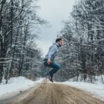 photo of man jumping on dirt road